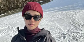 Di tengah salju, Yura tampil dengan jaket hitam dipadukan inner turtleneck warna maroon yang serasi dengan bennienya. Ia pun menambahkan kacamata hitam pada wajahnya yang tanpa makeup. Credit: Instagram (@yurayunita)