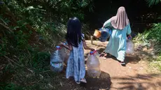 Seorang anak menemani ibunya Warga mengambir air dari satu-satunya sumber mata air di di Kampung Cijaura, Desa Cidokom, Bogor, Jawa Barat, Minggu (26/07/2026). (KLY/ Arie Basuki)