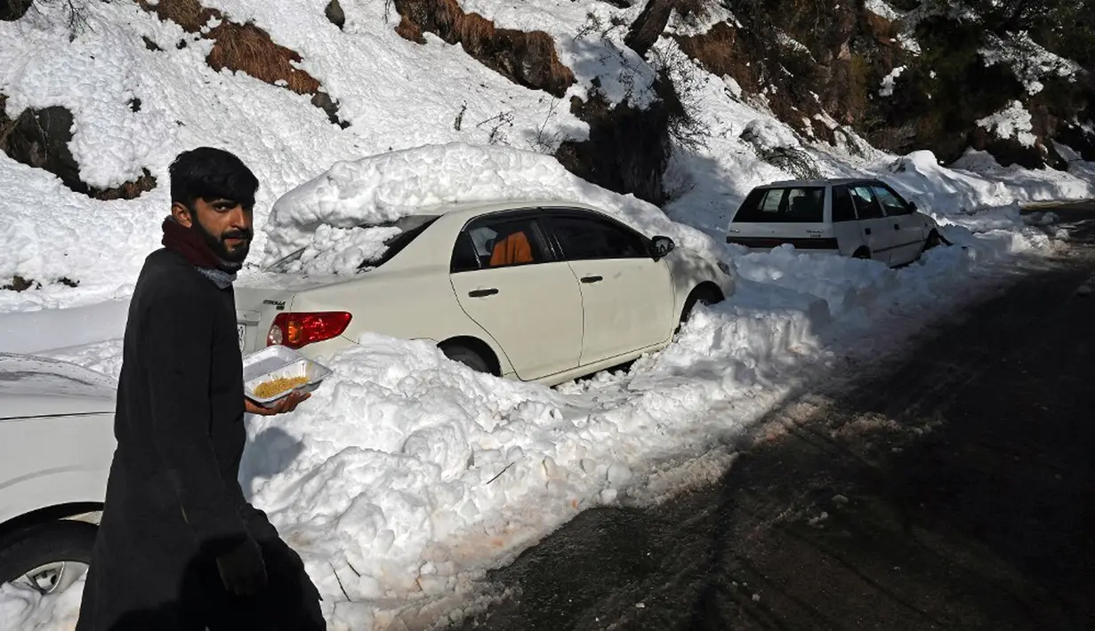 Seorang pria berjalan melewati kendaraan yang terjebak salju di sepanjang jalan Bukit Murree, Pakistan, 9 Januari 2022. Sebanyak 22 wisatawan tewas saat sekitar 1.000 kendaraan terjebak salju tebal di Bukit Murree. (Aamir QURESHI/AFP)