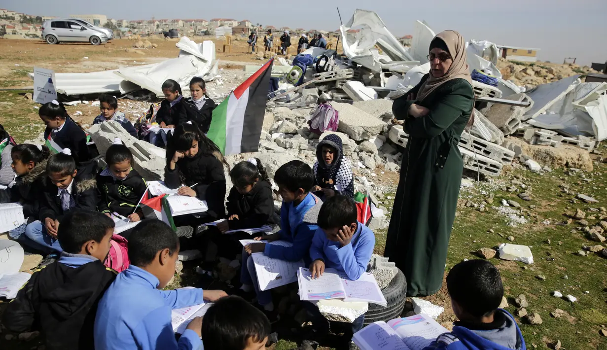 Anak-anak belajar di antara puing sekolah mereka yang hancur di Tepi Barat, Palestina, Minggu (4/2). Setidaknya 45 sekolah di Palestina tengah menghadapi ancaman kehancuran yang dilakukan oleh otoritas Israel. (AP Photo/Mahmoud Illean)
