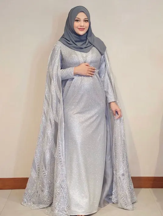 Kali ini, Aurelie Hermansyah tampil mengenakan gaun panjang berwarna abu-abu muda yang berkilauan dan detail cape dari organza yang dibordir bermotif. Ia sempurnakan penampilannya dengan gaya jilbab sederhana, yang juga berwarna abu-abu tua. Foto: Instagram.