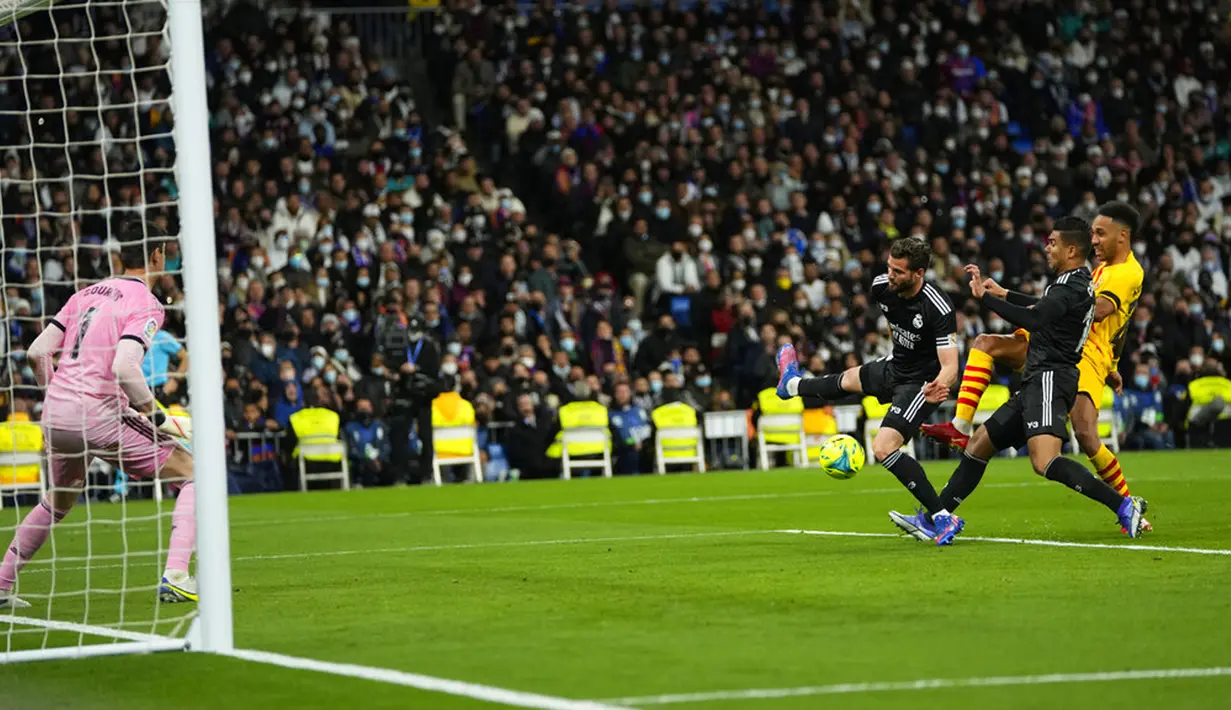 Pemain Barcelona Pierre-Emerick Aubameyang (kanan) menendang bola ke gawang di depan pemain Real Madrid Nacho (kedua kiri), Casemiro, dan kiper Thibaut Courtois pada pertandingan sepak bola La Liga Spanyol di Stadion Santiago Bernabeu, Madrid, Spanyol, Minggu (20/3/2022). (AP Photo/Manu Fernandez)