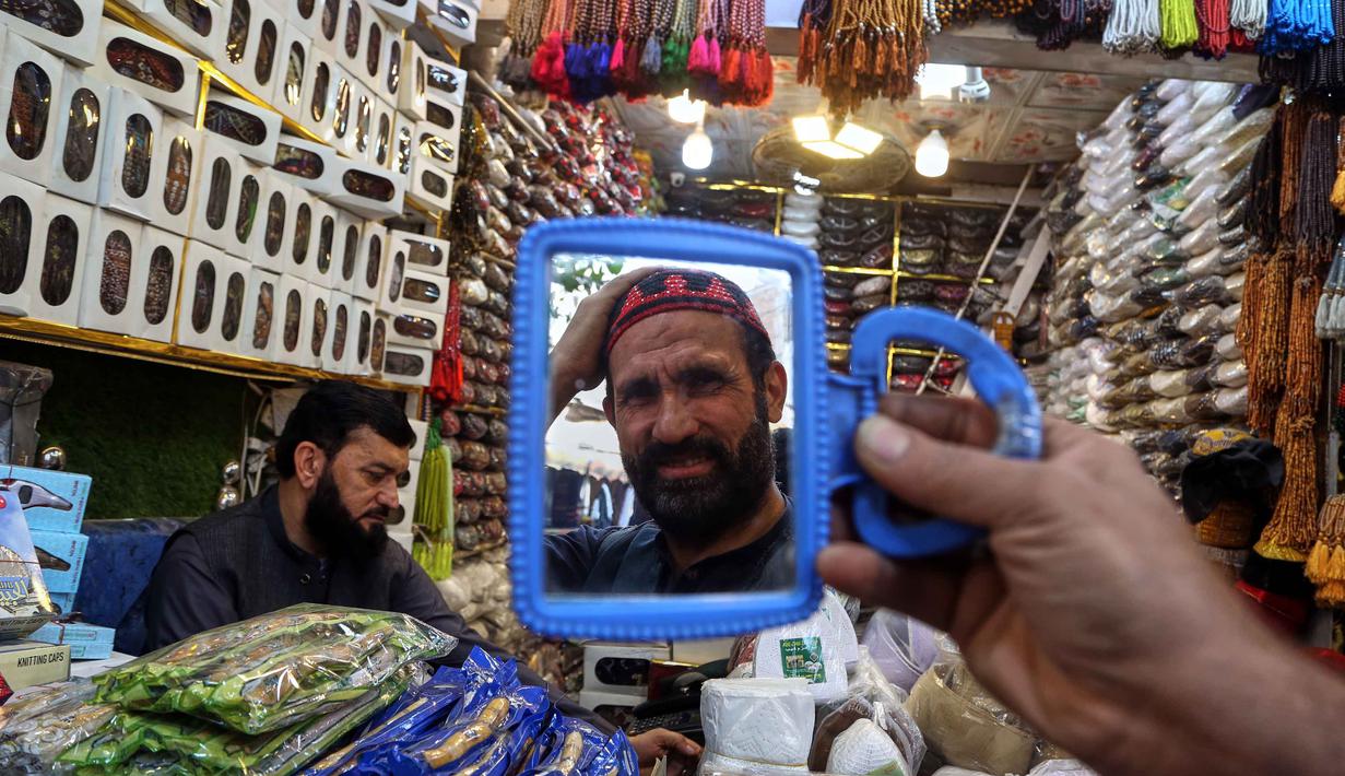 Rata-rata, mereka mencari bahan makanan, buah-buahan untuk berbuka puasa hingga pakaian. Tampak dalam foto, seorang pria mencoba topi tradisional yang akan digunakan saat berdoa selama bulan puasa Ramadan, di sebuah toko di Peshawar, Pakistan, Senin, 16 Februari 2026. (AP Photo/Muhammad Sajjad)