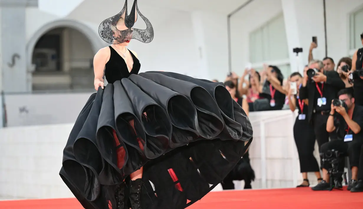 <p>Dalam tampilan dramatis yang mengingatkan kita pada couture Maleficent, Gaga berjalan di karpet merah dengan gaun hitam tebal Christian Dior yang menampilkan garis leher menjuntai dan rok bervolume. (Alberto PIZZOLI / AFP)</p>