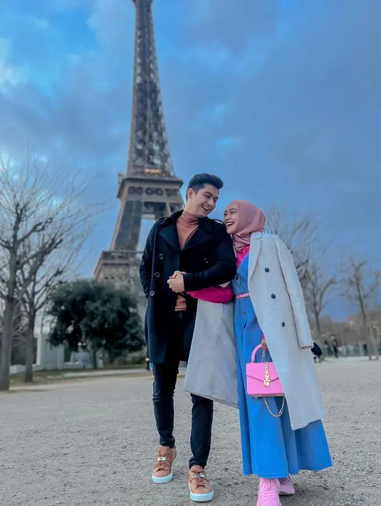 Dress Overall jeans dan kemeja shocking pink untuk gaya cute di Paris. Dilengkapi dengan sneaker dan tas berwarna senada plus coat yang disampirkan di punggung untuk menambah gaya (Foto: Instagram @riaricis1795)