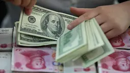 Teller menghitung uang pecahan 100 Dollar di atas uang yuan China di sebuah bank di Huaibei, China, 11 Agustus 2015. Langkah Bank Sentral China menurunkan nilai tukar yuan terhadap dolar AS langsung membuat pelaku pasar ketakutan. (REUTERS/Stringer)