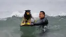 Michael Uy memegangi anjingnya saat akan mengikuti kompetisi kontes surfing anjing Petco Unleashed ke-10 di pantai Imperial, California, 1 Agustus 2015. (REUTERS/Mike Blake)