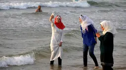 Seorang wanita berselfie di tepi pantai Laut Mediterania, Tel Aviv, Israel (30/8). Para wanita hijab ini tetap santai di tengah keramaian wanita berbikini. (REUTERS / Baz Ratner)
