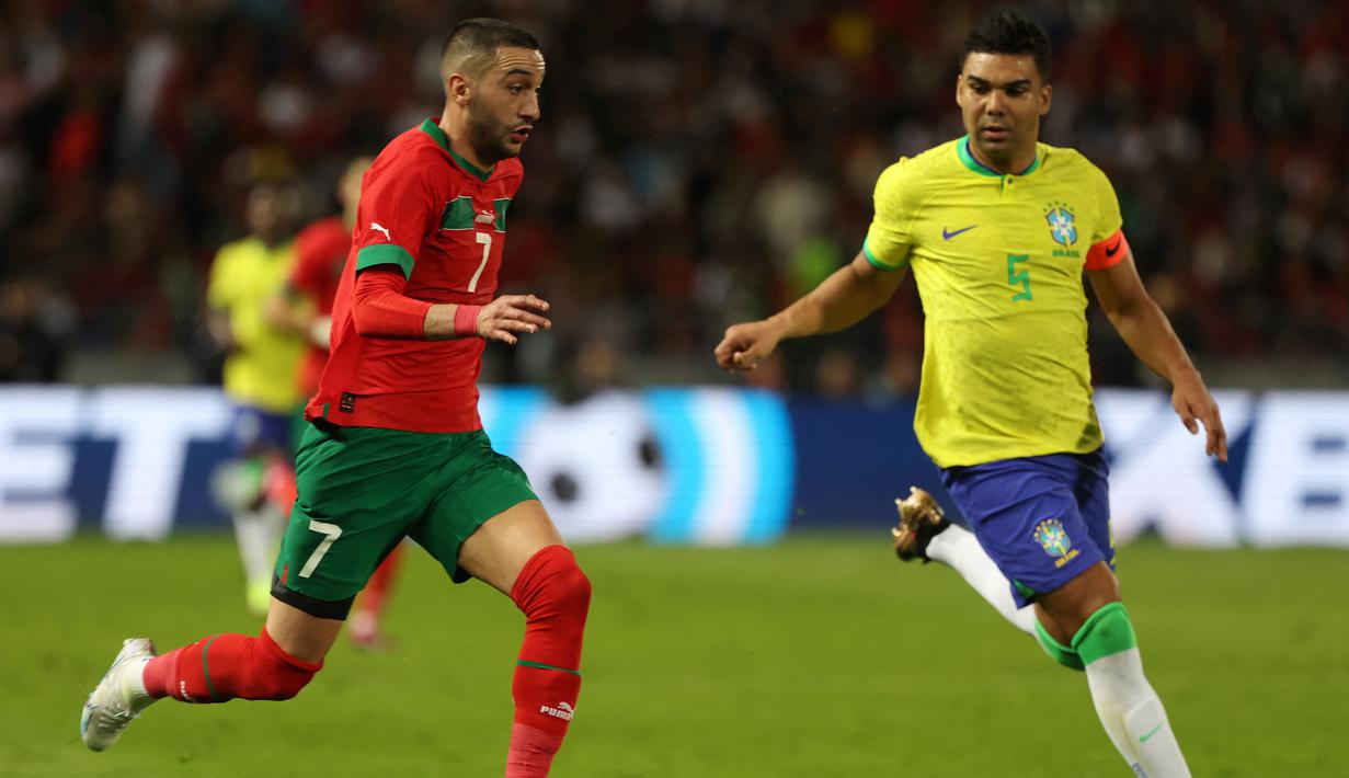 Gelandang Timnas Brasil, Casemiro (kanan) membayangi pergerakan gelandang Maroko, Hakim Ziyech pada laga persahabatan FIFA Matchday di Ibn Batouta Stadium, Tangier, Maroko (26/3/2023). Tampil sebagai kapten tim dan bermain penuh selama 90 menit, Casemiro gagal membawa Brasil terhindar dari kekalahan 1-2 meski ia mampu menyumbang satu-satunya gol untuk Timnas Brasil. (AFP/Fadel Senna)