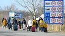 Keluarga Ukraina yang melarikan diri dari konflik di negara mereka sehari setelah Rusia melancarkan serangan militer berjalan dengan barang bawaan mereka setelah melintasi perbatasan Hungaria-Ukraina dekat Beregsurany, Hungaria (25/2/2022). (AFP/Attila Kisbenedek)