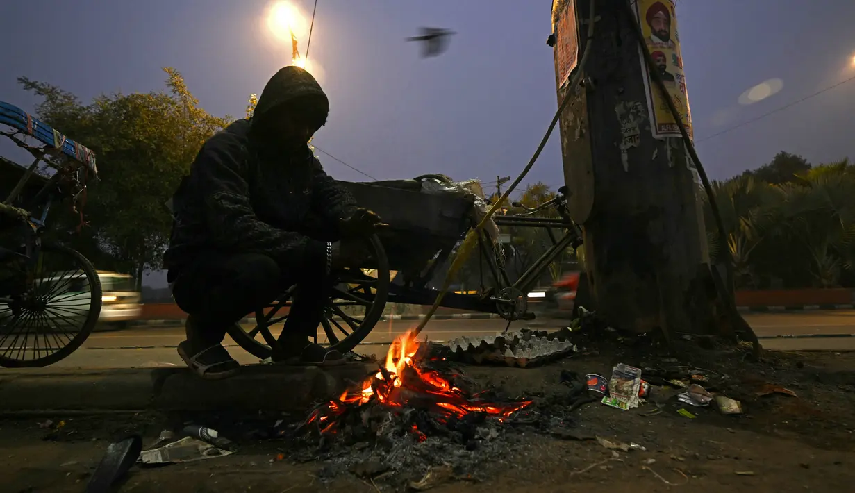Mereka menghangatkan diri di sekitar api yang membara yang dibangun dari sampah dan kotak kardus yang dibuang. (Money SHARMA / AFP)