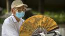 Seorang pria tua yang mengenakan masker mengipasi dirinya sendiri di sebuah taman umum di Beijing, Jumat (8/7/2022). Ibu kota China, Beijing, tampaknya telah membatalkan rencana untuk mengeluarkan mandat yang mengharuskan orang menunjukkan bukti vaksinasi COVID-19 untuk masuk ke ruang publik tertentu setelah penolakan di kalangan penduduk. (AP Photo/Mark Schiefelbein)