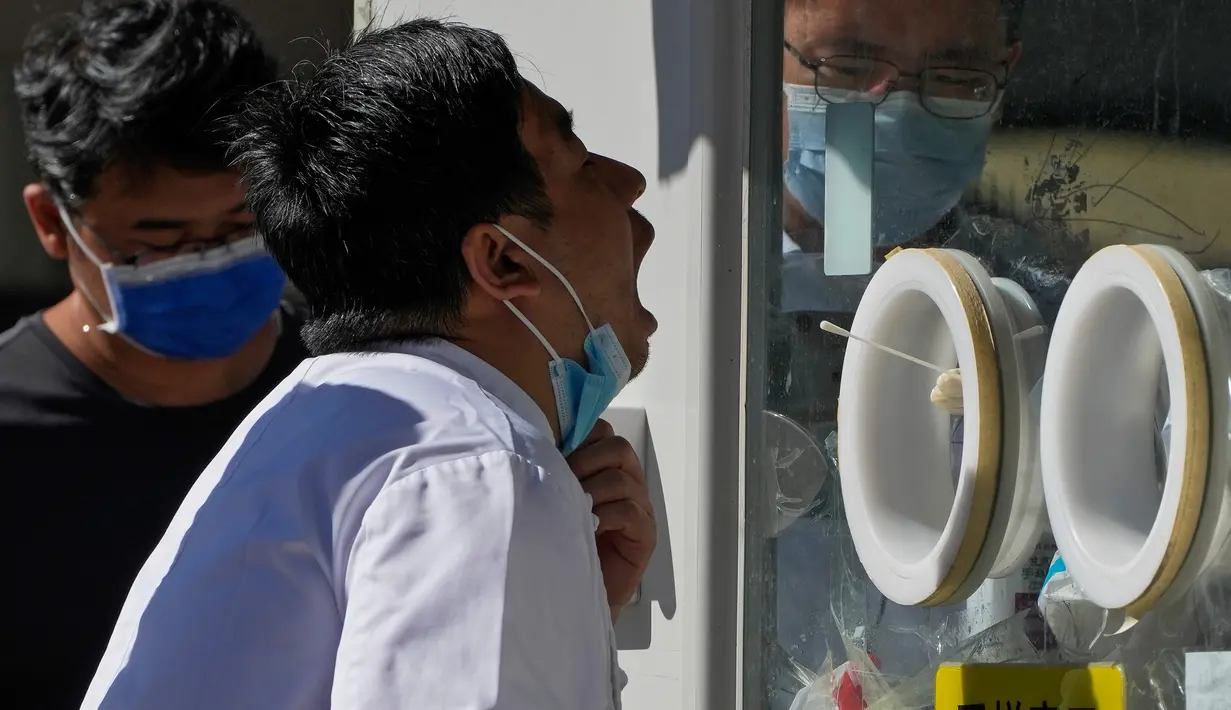 Seorang pria membuka maskernya untuk melakukan swab tenggorokan COVID-19 secara rutin di tempat pengujian virus corona di Beijing, Selasa (6/9/2022). Saat ini ada 33 kota di China yang berada dalam situasi lockdown sebagian atau penuh karena wabah COVID-19. (AP Photo/Andy Wong)