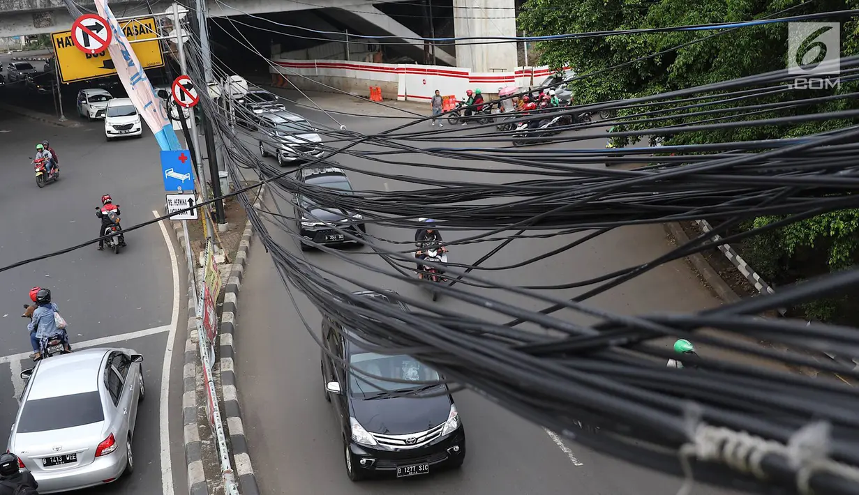 Kendaraan melintas di bawah Instalasi kabel menjuntai di Jalan Dewi Sartika, Jakarta Timur, Sabtu (19/1). Selain mengganggu keindahan kota, kondisi tersebut juga berbahaya karena dapat memicu hubungan pendek arus listrik. (Liputan6.com/Immanuel Antonius)