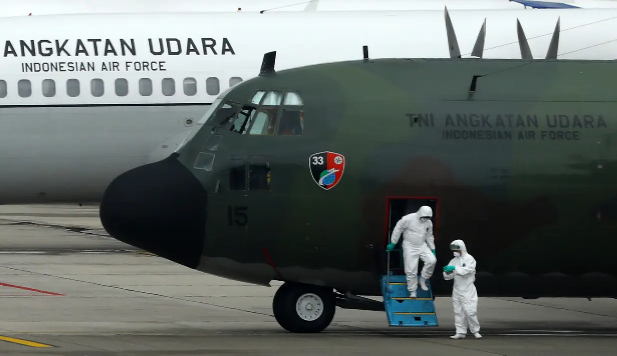 Petugas mengenakan pakaian pelindung turun dari pesawat hercules saat tiba bandara internasional Hang Nadim, Batam, Minggu (2/2/2020). Ada tiga pesawat disiapkan Hercules C130 dan dua pesawat Boeing 737-400 yang juga milik TNI AU untuk WNI dari Wuhan menuju ke Natuna. (AFP/Ricky Prakoso)