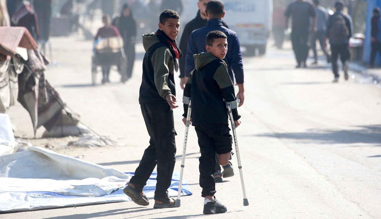Rateb Mahmoud Qaliq sempat menggunakan kaki palsu, namun ia jarang menggunakannya karena tidak nyaman. Rateb Mahmoud Qaliq merasa nyaman menggunakan kruk karena lebih ringan. Tampak dalam foto, Rateb Mahmoud Qaliq (kiri) bersam rekannya di Deir al-Balah, di Jalur Gaza tengah, pada 3 Desember 2025. (Bashar Taleb/AFP)