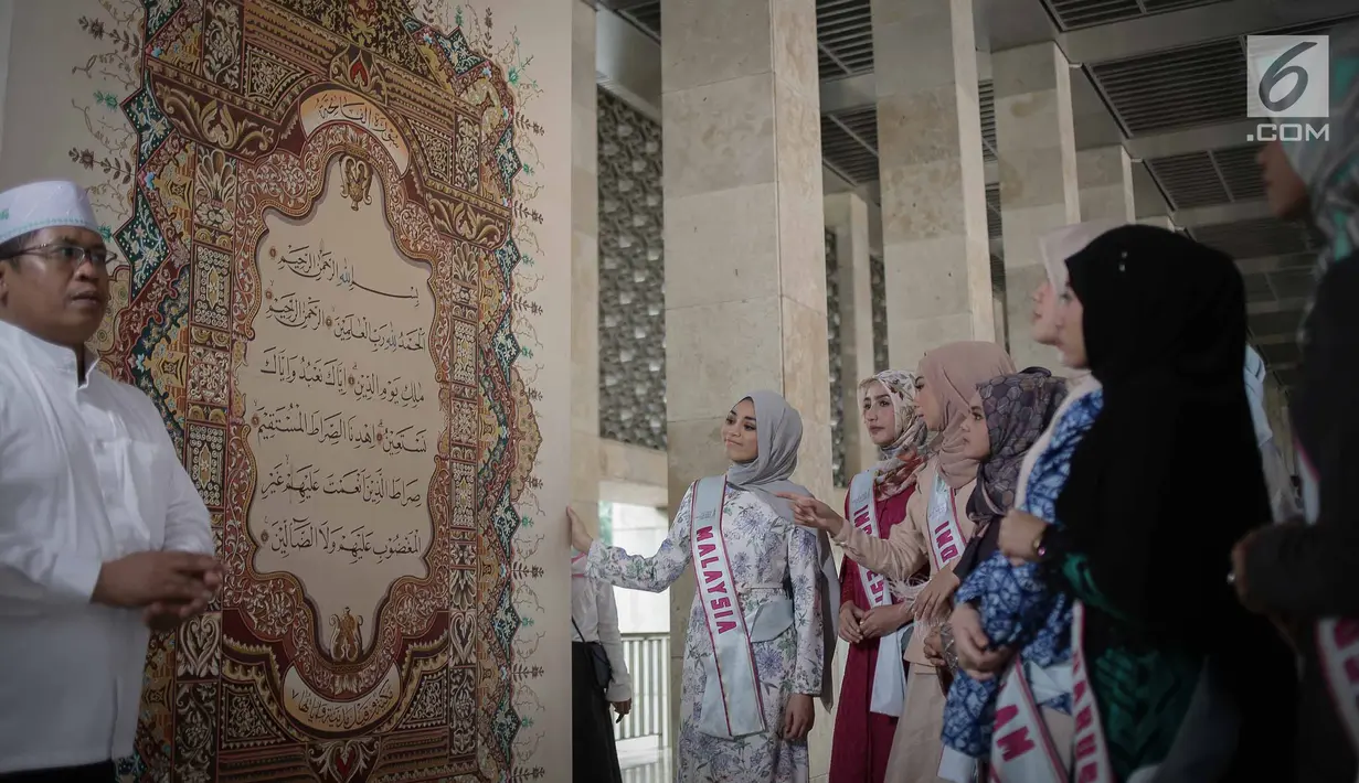 Kepala Protokol Masjid Istiqlal, Abu Hurairah menunjukkan kaligrafi Al-Quran kepada peserta Puteri Muslimah Asia 2018 di Mesjid Istiqlal, Jakarta, Kamis (3/4).  Kegiatan tersebut diikuti perwakilan sejumlah negara Asia. (Liputan6.com/Faizal Fanani)
