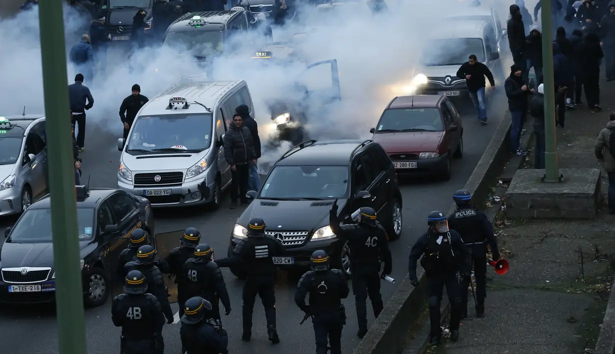 Polisi anti huru-hara mengamankan aksi pengemudi taksi yang memblokir jalan dengan membakar ban saat unjuk rasa menentang layanan transportasi VTC seperti Uber, di jalan lingkar di porte Maillot di Paris, Perancis, Selasa (26/1). (AFP PHOTO/Thomas SAMSON)