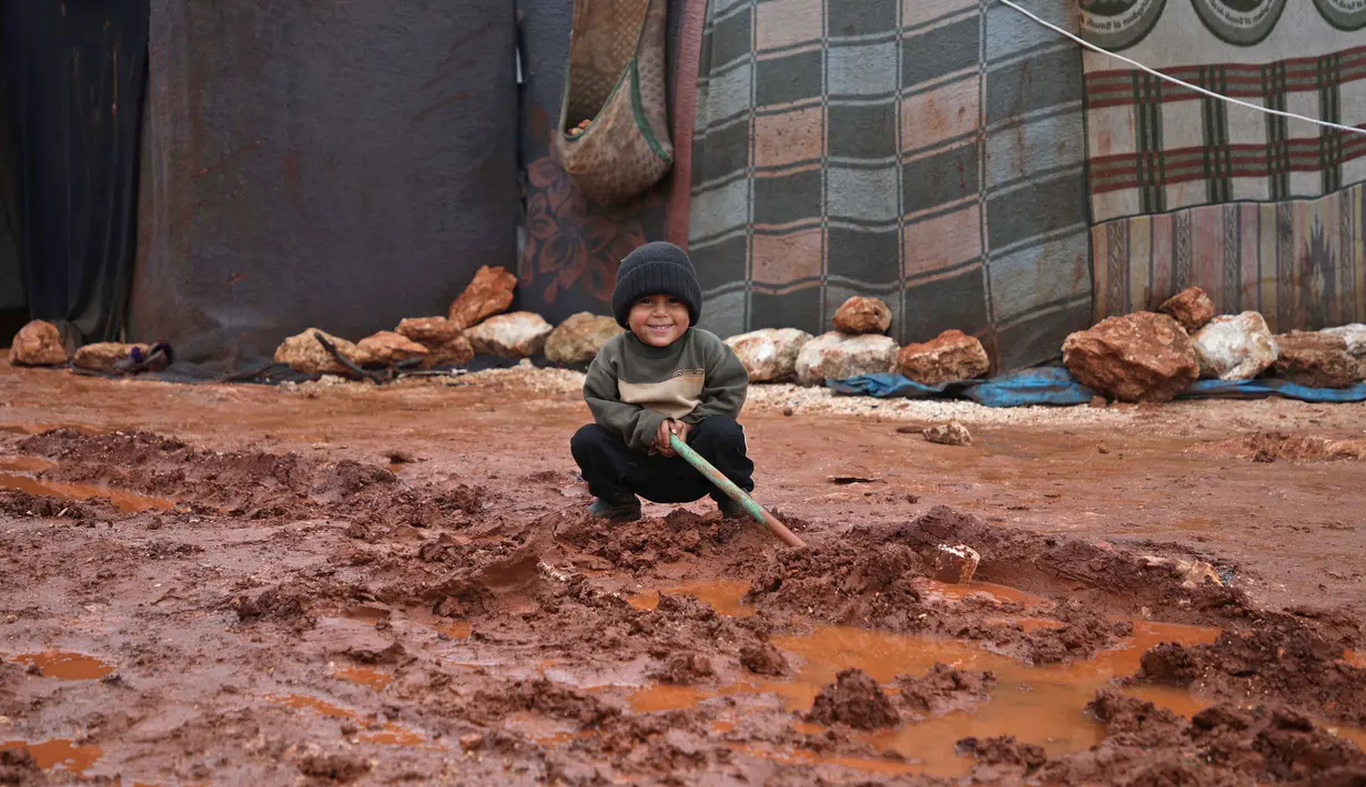 Seorang anak tersenyum saat banjir menggenangi lokasi pengungsian di Kamp Cordoba, Batabu, Idlib, Suriah, Rabu (16/1). Hujan badai membuat kamp pengungsian mereka kebanjiran. (Aaref Watad/AFP)