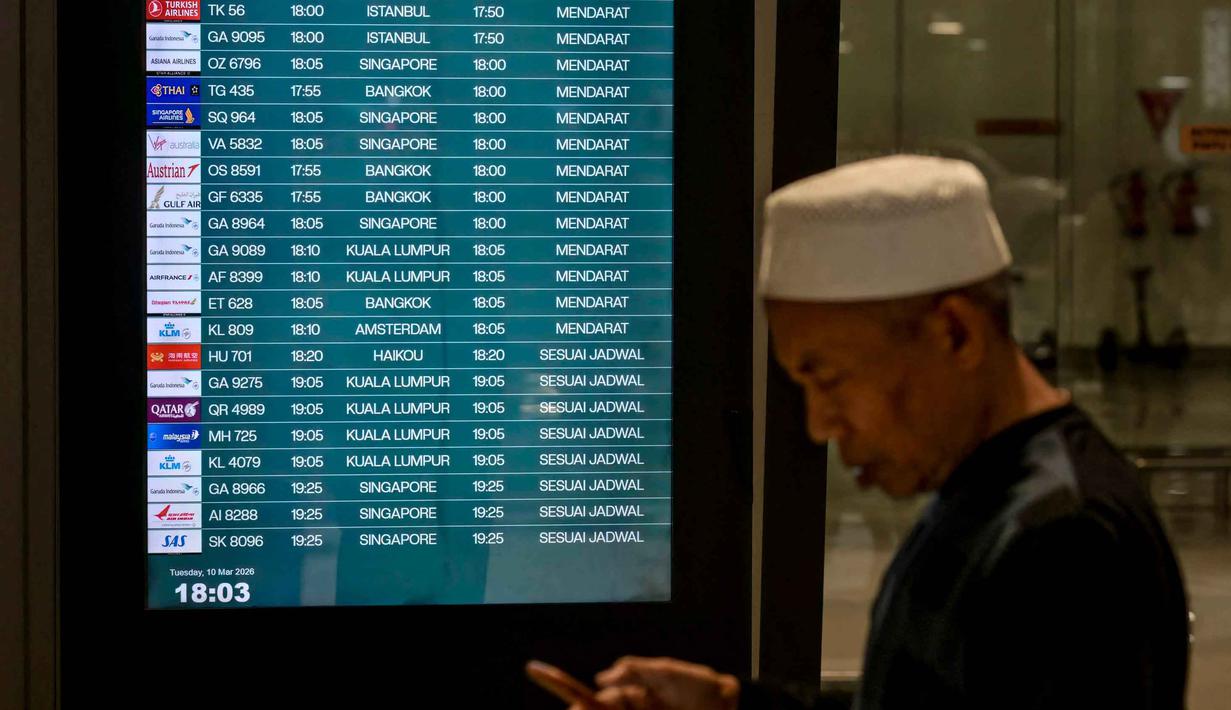 Perubahan jadwal penerbangan imbas ketegangan antara Amerika Serikat-Israel dengan Iran yang berdampak pada lalu lintas udara internasional. Tampak dalam foto, seorang pria menggunakan ponsel pintarnya sambil berjalan melewati papan informasi penerbangan saat Warga Negara Indonesia yang kembali dari Iran tiba di Bandara Internasional Soekarno-Hatta, Tangerang, Banten, pada Selasa 10 Maret 2026. (BAY ISMOYO/AFP)