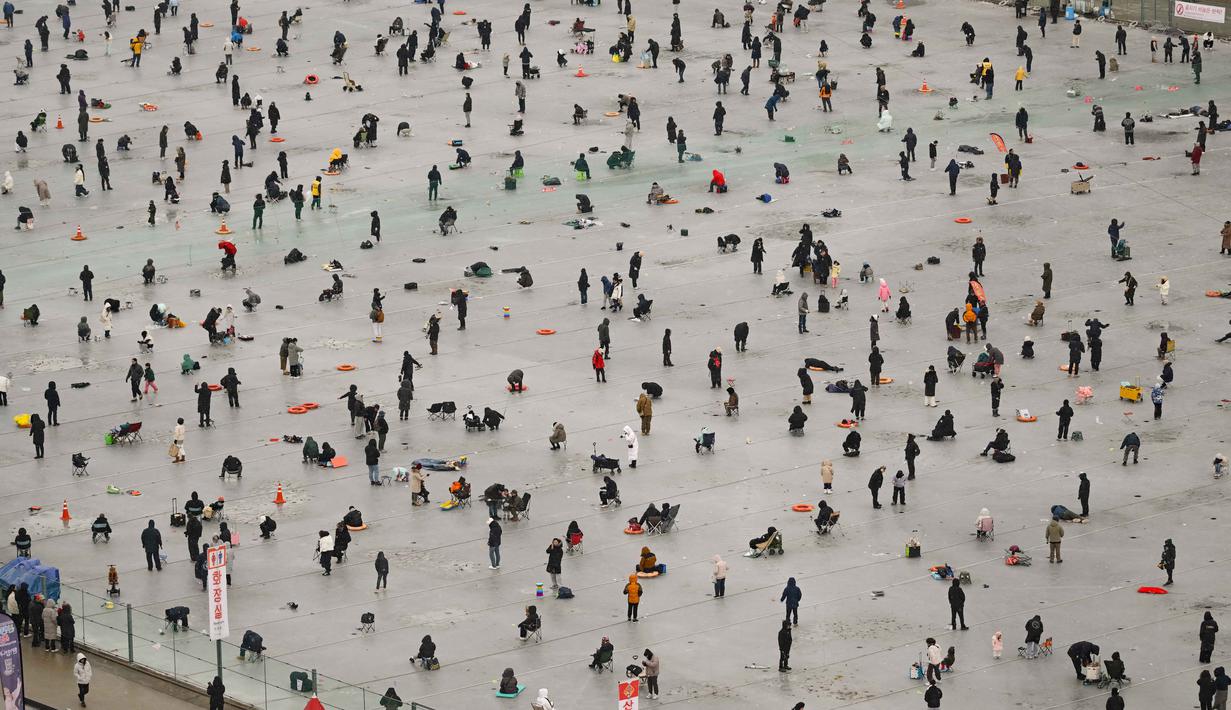 Selain memancing di atas es, pengunjung dapat mencoba menangkap ikan dengan tangan kosong, meluncur dengan kereta salju (sledding), bobsled, hingga mengunjungi alun-alun patung es dalam ruangan terbesar di dunia. Tampak dalam foto, orang-orang memancing melalui lubang-lubang di sungai yang membeku selama festival tahunan memancing di atas es, Hwacheon, Korea Selatan, pada Sabtu 10 Januari 2026. (Shin Yong-ju/AFP)