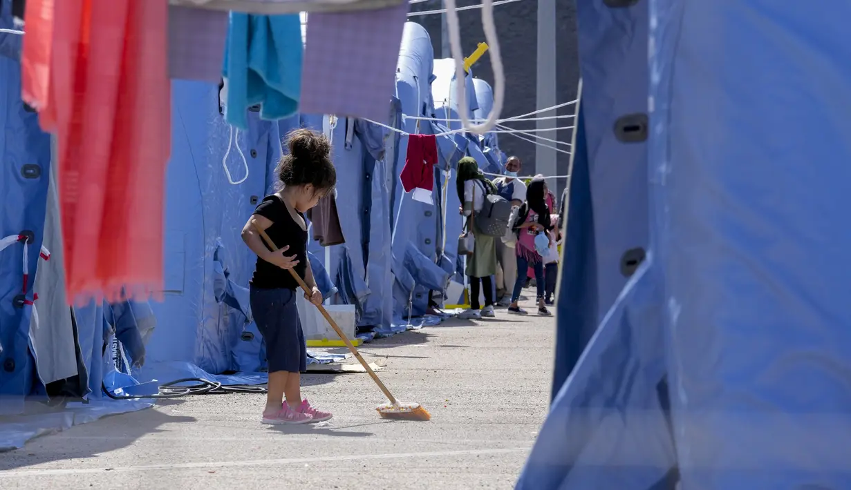 Seorang anak Afghanistan menyapu di kamp pengungsian Palang Merah Italia, Avezzano, Italia, Selasa (31/8/2021). Kamp karantina ini menampung 1.250 imigran. (AP Photo/Andrew Medichini)