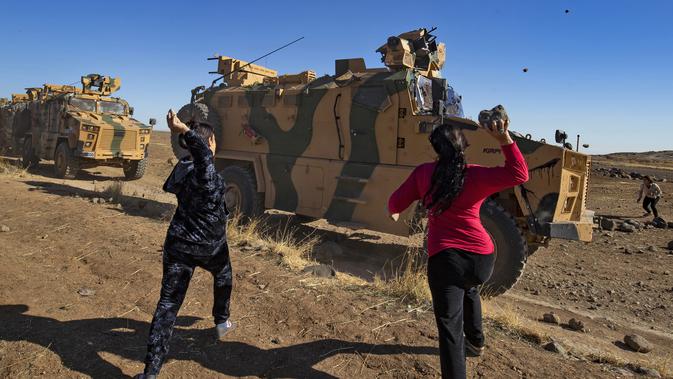 Dua wanita Kurdi melemparkan batu ke kendaraan militer Turki di dekat kota Al-Muabbadah, bagian timur laut Hassakah, Suriah (8/11/2019). Pelemparan batu terjadi saat militer Turki melakukan konvoi dengan militer Rusia. (AFP/Delil Souleiman)
