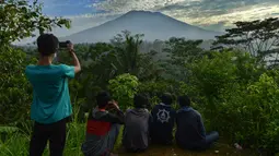 Warga melihat Gunung Agung di Karangasem di pulau resor Bali, Indonesia (24/9). Gunung Agung adalah gunung berapi yang besar dengan puncak 3.142 meter di atas permukaan laut. Gunung ini mendominasi pemandangan timur Bali. (AFP Photo/Sonny Tumbelaka)