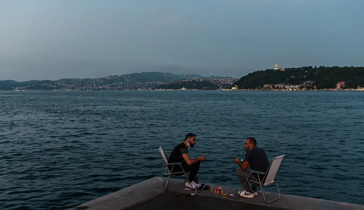 Orang-orang menikmati malam di sebelah pantai Bosphorus ketika jembatan Fatih Sultan Mehmet terlihat di Istanbul (6/7/2020). Jembatan Fatih Sultan Mehmet, yang dikenal dengan sebutan Jembatan Bosporus Kedua, adalah sebuah jembatan di Istanbul, Turki yang melintasi selat Bosporus. (AFP/Ozan Kose)