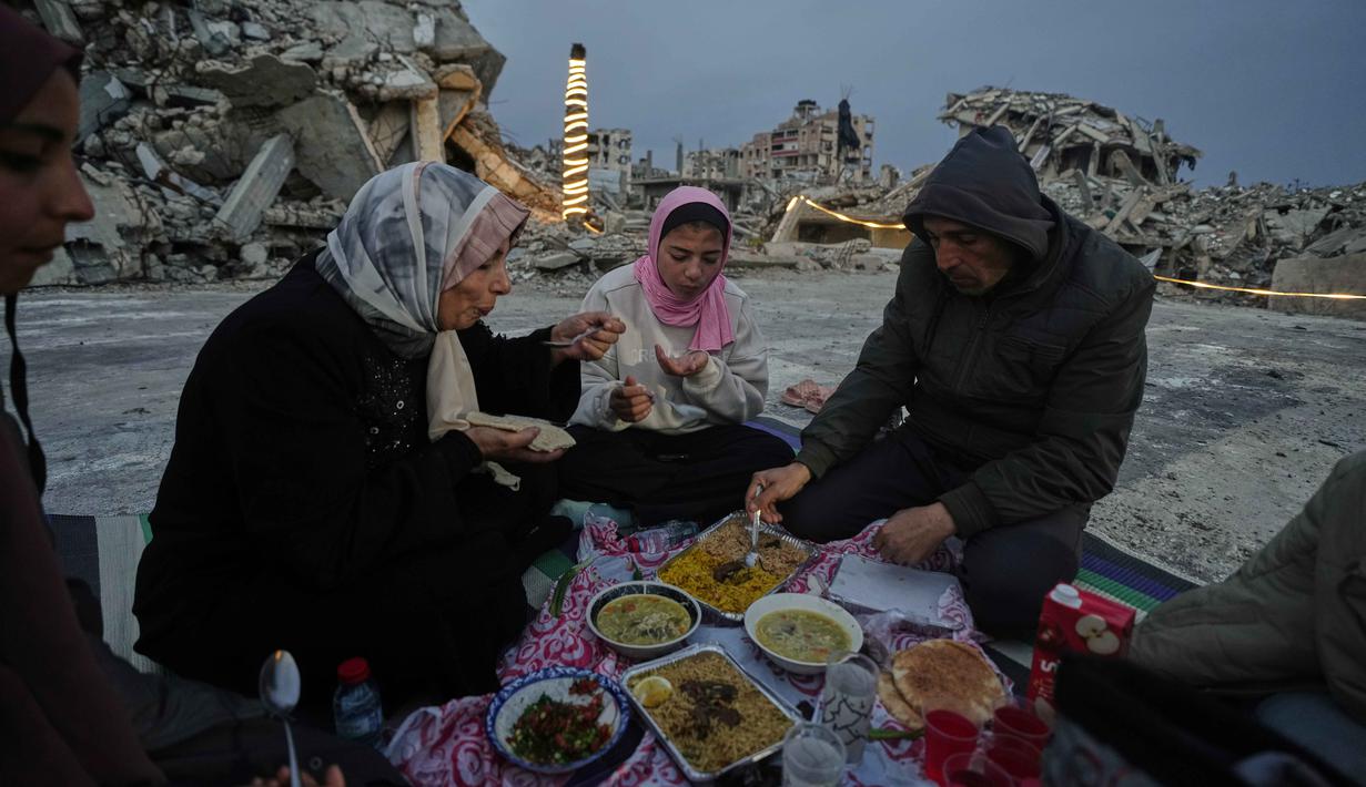 Anggota keluarga Al-Najar berbuka puasa selama bulan suci Ramadan di tengah reruntuhan bangunan yang hancur di Kota Gaza, Jumat 13 Maret 2026. Di tengah puing-puing bangunan yang nyaris rata dengan tanah, masyarakat Gaza tetap menjaga nuansa hangat kebersamaan Ramadan seperti biasanya. (AP Photo/Jehad Alshrafi)