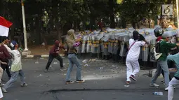 Massa melempar batu ke arah polisi yang membentuk barikade dengan tameng di sekitaran Gedung DPR RI, Jakarta, Senin (30/9/2019). Kericuhan pecah lantaran massa yang kebayakan terdiri dari pelajar tersebut berusaha masuk ke area depan DPR. (Liputan6.com/Angga Yuniar)