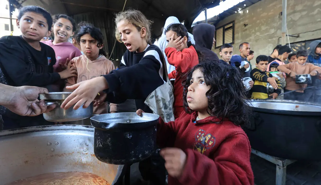 Situasi ini menempatkan pengungsi Palestina berada di ambang kelaparan. Tampak dalam foto, anak-anak pengungsi Palestina menunggu untuk menerima makanan dari dapur amal di kamp pengungsi Nuseirat, Jalur Gaza Tengah pada 13 April 2026. (Eyad Baba/AFP)