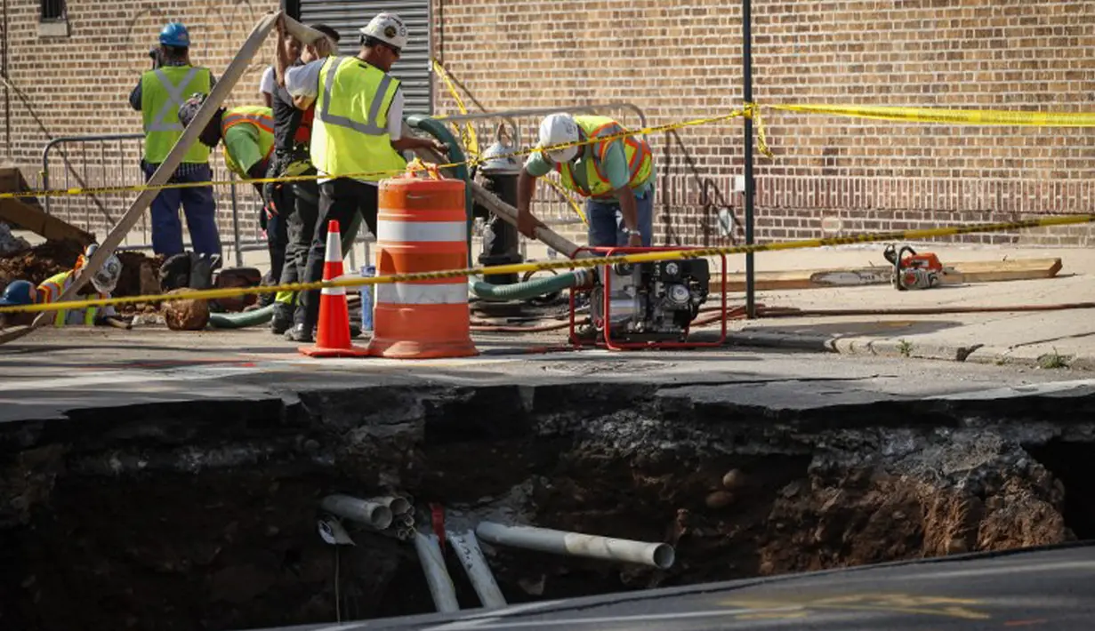 Sejumlah petugas bekerja di dekat lubang besar (sinkhole) di wilayah Brooklyn, New York, Selasa (4/8/2015). Lubang yang terbentuk di persimpangan pemukiman Sunset Park itu disebabkan erosi dan merusak pipa air serta aspal jalan. (AFP/Kena Betancur)