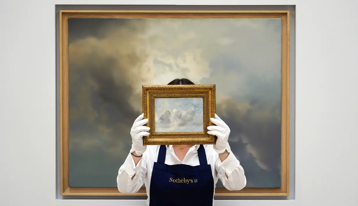 Seorang staf memegang lukisan 'Cloud Study' karya John Constable dengan latar belakang 'Study for Clouds' karya Gerhard Richter di Sotheby's, London, Inggris, 22 Juni 2022. Lukisan yang akan dilelang pada 29 Juni 2022 itu diperkirakan memiliki harga 100.000-150.000 pound, sedangkan 'Study for Clouds' 6-8 juta pound. (AP Photo/Alberto Pezzali)