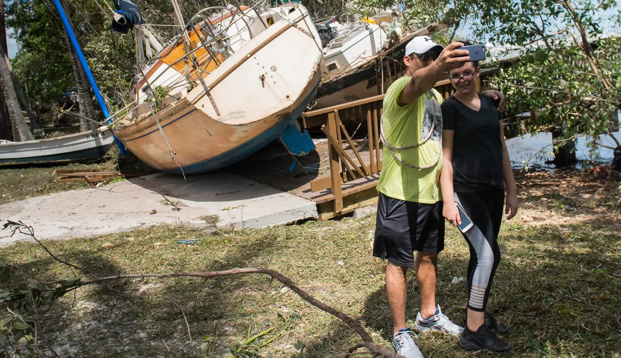 Sepasang warga berswafoto dengan latar belakang kapal yang terhempas ke daratan akibat terhempas badai Irma di Coconut Grove, Florida, Senin (11/9). Badai Irma menghantam negara bagian Florida dengan kecepatan angin mencapai 200 km/jam. (SAUL LOEB/AFP)