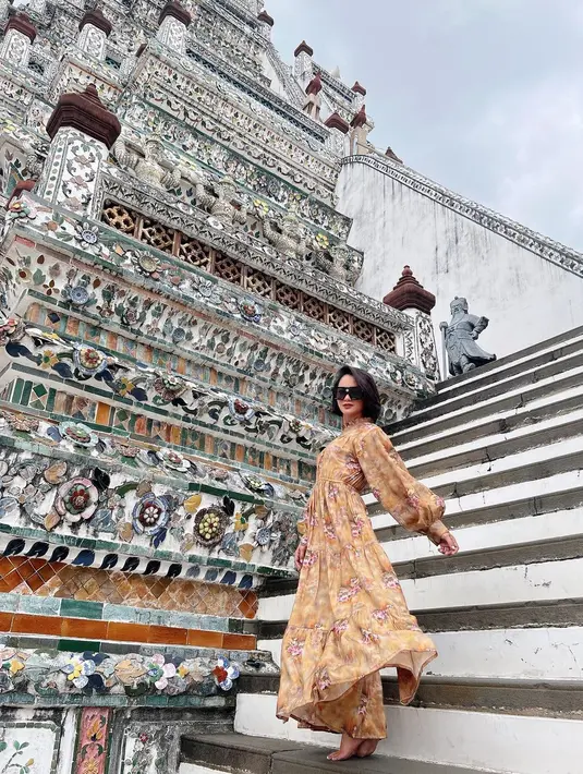 Ririn Ekawati tampil memesona berbalut dress floral warna coklat dengan detail puff sleeve saat berpose di tangga selama liburan di Thailand.  (Instagram/ririnekawati)