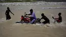 Bocah laki-laki membantu pengendara sepeda motor yang berusaha menyeberangi sungai di Les Anglais, 10 Oktober 2016. Selain merusak ribuan rumah, badai Matthew di Haiti juga memutus jembatan yang biasa digunakan warga. (REUTERS/Andres Martinez Casares)