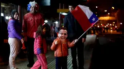 Seorang anak membawa bendera Chile sambil memakai topeng penyerang Chile, Alexis Sanchez merayakan kemenangan Chile di Copa America 2015 di Santiago, Chile, (25/6/2015). Chile melaju ke semifinal usai mengalahkan Uruguay 1-0. (REUTERS/Pablo Sanhueza)
