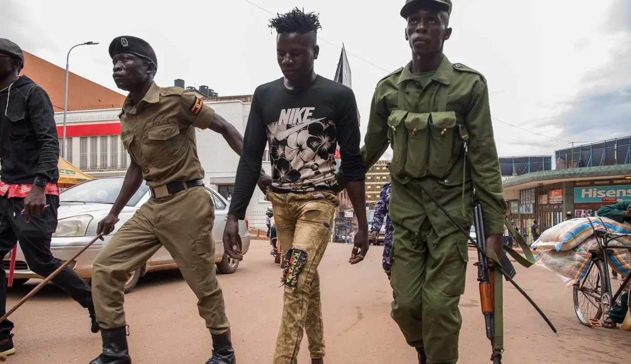 Aparat kepolisian menangkap pemuda yang masih berkeliaran di Kampala, Uganda (26/3/2020). Pemerintah setempat juga menutup seluruh pintu perbatasan, kecuali untuk barang terbatas dan penerbangan darurat resmi sebagai upaya menekan penyebaran Covid-19. (AFP/Badru Katumba)