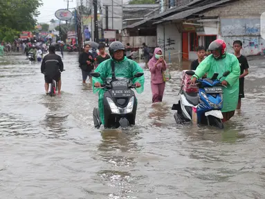 Warga berusaha melintasi genangan air ketika banjir merendam Jalan KH. Hasyim Ashari, Tangerang, Banten, Sabtu (16/7/2022). Akibat luapan kali angke ruas jalan yang menghubungkan Tangerang-Jakarta itu terputus akibat banjir. (Liputan6.com/Angga Yuniar)