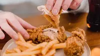 Seseorang sedang makan ayam kentucky yang disajikan bersama kentang goreng dengan tangan. (Liputan6.com/Pexels/Tim Samuel)
