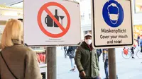 Para pejalan kaki berjalan melewati tanda yang mengingatkan warga untuk memakai masker dan larangan mengonsumsi alkohol di Munich, Jerman (11/12/2020). Kasus penularan dan kematian harian COVID-19 di Jerman terus meningkat dan mencapai rekor tertinggi baru. (Xinhua/Philippe Ruiz)