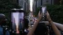 Orang-orang mengambil gambar saat matahari terbenam di Manhattan ketika fenomena "Manhattanhenge" di 42nd street, New York, Senin (11/7/2022). Fenomena Manhattanhenge hanyaterjadi di musim panas, tepatnya diantara bulan Mei hingga Juli. (Yuki IWAMURA / AFP)