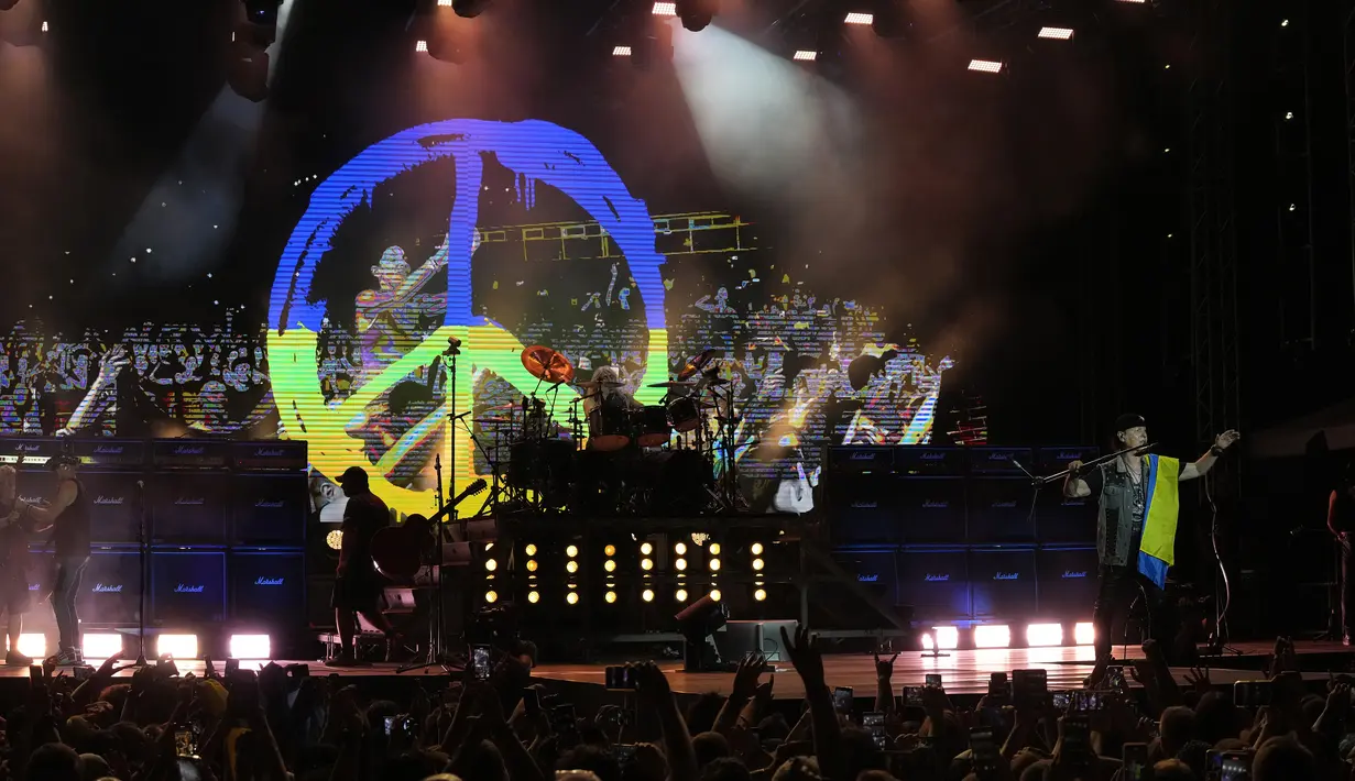 Aksi vokalis Scorpions, Klaus Meine (kanan) memegang bendera Ukraina dengan latar belakang layar besar tanda Perdamaian dalam warna bendera Ukraina yang ditampilkan selama konser di Stadion Tsirion Limassol, Siprus, Selasa (12/7/2022). (AP Photo/Petros Karadjias)