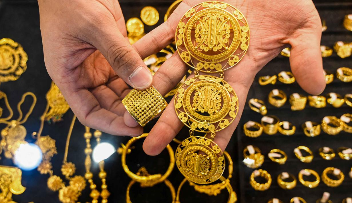 Seorang karyawan memegang beberapa perhiasan emas di sebuah toko perhiasan di Banda Aceh pada Rabu 14 Januari 2026. Pada Rabu (14/1/2026), harga emas dan perak terus menguat mencapai level tertinggi. (CHAIDEER MAHYUDDIN/AFP)