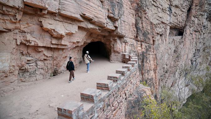 Wisatawan menyusuri jalur di tebing dekat Waduk Xiagou yang berada di Chaiguan, Kota Shahe, Provinsi Hebei, China utara, pada 28 Oktober 2020. Jalur tebing pada dinding Waduk Xiagou ini digali secara manual pada 1970-an. (Xinhua/Mu Yu)