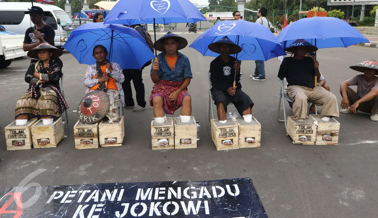 Sambil menggunakan payung, Petani Kendeng menyemen kaki saat menggelar aksinya di depan Istana Negara, Jakarta, Selasa (14 /3). Aksi ini sebagai bentuk penolakan terhadap Keputusan Gubernur Jawa Tengah Nomor 660.1/6 Tahun 2017. (Liputan6.com/Helmi Afandi)