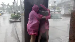Dua wanita berlindung di dinding untuk menghindari angin kencang yang disebabkan topan Dujuan di Taipei, Taiwan, Senin (28/9). Ribuan orang diungsikan untuk menghadapi topan raksasa Dujuan yang diprediksikan akan menyerang Taiwan.(REUTERS/Pichi Chuang)