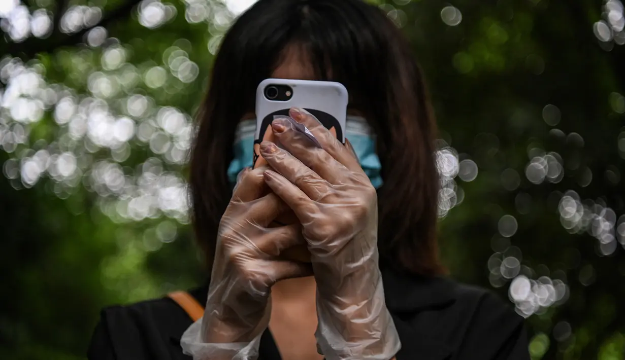 Seorang warga mengenakan masker dan sarung tangan menunggu dalam barisan untuk tes virus corona di lingkungan di Wuhan, provinsi Hubei, Jumat (15/5/2020). Pihak berwenang Kota Wuhan menggelar tes massal terhadap 11 juta warganya untuk mencegah gelombang kedua pandemi Covid-19. (Hector RETAMAL/AFP)