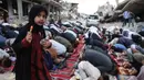 Seorang gadis memegang sepotong permen berdiri di antara warga Palestina yang melaksanakan salat menandai dimulainya Idul Adha, Hari Raya Kurban, di jalan yang rusak parah di Khan Yunis, Jalur Gaza Selatan, pada Rabu 27 Mei 2026. (BASHAR TALEB/AFP)